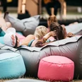 Hörspielwiese Cologne The picture shows people lying relaxed on colorful beanbags in the open air at the Hörspielwiese. A stage can be seen in the background, creating a relaxed and cozy atmosphere.