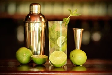 Cocktail - Workshop an der Bar A mojito cocktail with limes, mint and a cocktail shaker on a bar, softly lit.