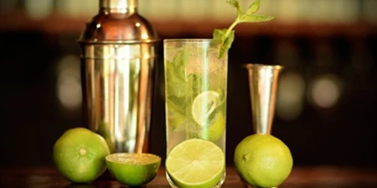 Cocktail - Workshop an der Bar Ein Mojito-Cocktail mit Limetten, Minze und einem Cocktailshaker auf einer Bar, sanft beleuchtet.A mojito cocktail with limes, mint and a cocktail shaker on a bar, softly lit.