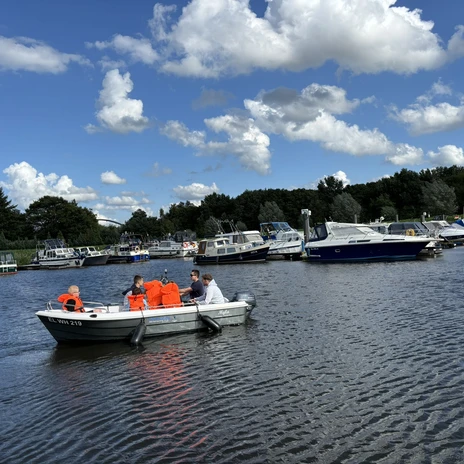 WasserheldenEmsland1.jpg Menschen mit Schwimmwesten auf Boot im Hafen, rundum ruhiges Wasser und Boote unter blauem Himmel