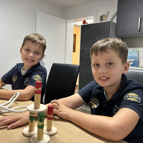 WasserheldenEmsland3.jpg Zwei Kinder sitzen am Tisch, basteln mit Holzbausteinen und lächeln in einer hellen Wohnung.