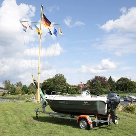 WasserheldenEmsland12.jpg Motorboot auf Anhänger steht auf einer Wiese am Hafen, daneben Flaggenmast und Boote im Wasser.