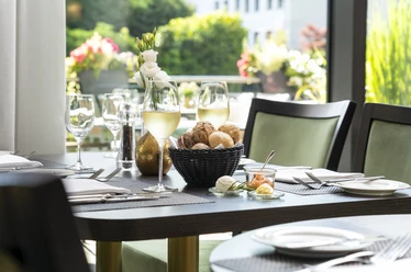 Weeken-Brunch - Im exklusiven Raum The picture shows a stylishly laid table with a bread basket and wine glasses in a light-flooded room. The background is decorated with floral arrangements that create an inviting and elegant atmosphere.