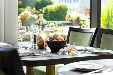 Weeken-Brunch - Im exklusiven Raum The picture shows a stylishly laid table with a bread basket and wine glasses in a light-flooded room. The background is decorated with floral arrangements that create an inviting and elegant atmosphere.