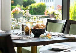Weeken-Brunch - Im exklusiven Raum The picture shows a stylishly laid table with a bread basket and wine glasses in a light-flooded room. The background is decorated with floral arrangements that create an inviting and elegant atmosphere.