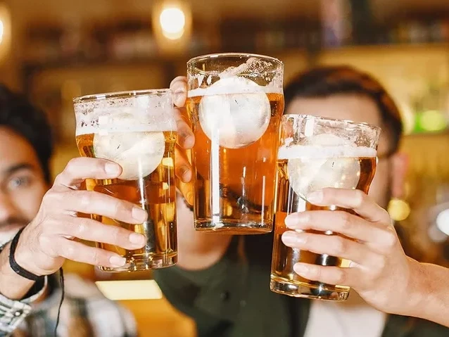 Kölscher Abend - Im Römerkeller Drei Menschen stoßen mit Biergläsern an, die Schaumkrönchen tragen, in gemütlicher Bar-Atmosphäre.Three people clink glasses of beer topped with foam in a cozy bar atmosphere.