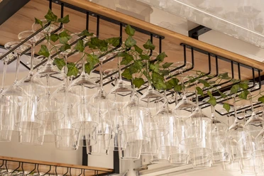 Gourmet Festival The picture shows elegantly arranged wine glasses hanging upside down on a wooden rack, decorated with fresh ivy vines in the background.