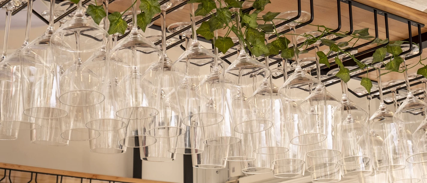 Gourmet Festival The picture shows elegantly arranged wine glasses hanging upside down on a wooden rack, decorated with fresh ivy vines in the background.