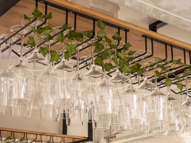 Gourmet Festival The picture shows elegantly arranged wine glasses hanging upside down on a wooden rack, decorated with fresh ivy vines in the background.