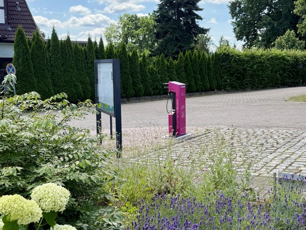 fahrrad-service-station-bispingen-touristik.jpg Eine Fahrrad-Service-Station steht auf einem gepflasterten Platz neben Schildern und grünen Hecken.