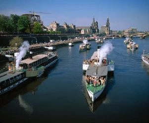 Dampferparade in Dresden Steamship parade in Dresden.jpg Dampfschiffe fahren auf der Elbe in Dresden, gesäumt von Zuschauern und historischer Architektur.