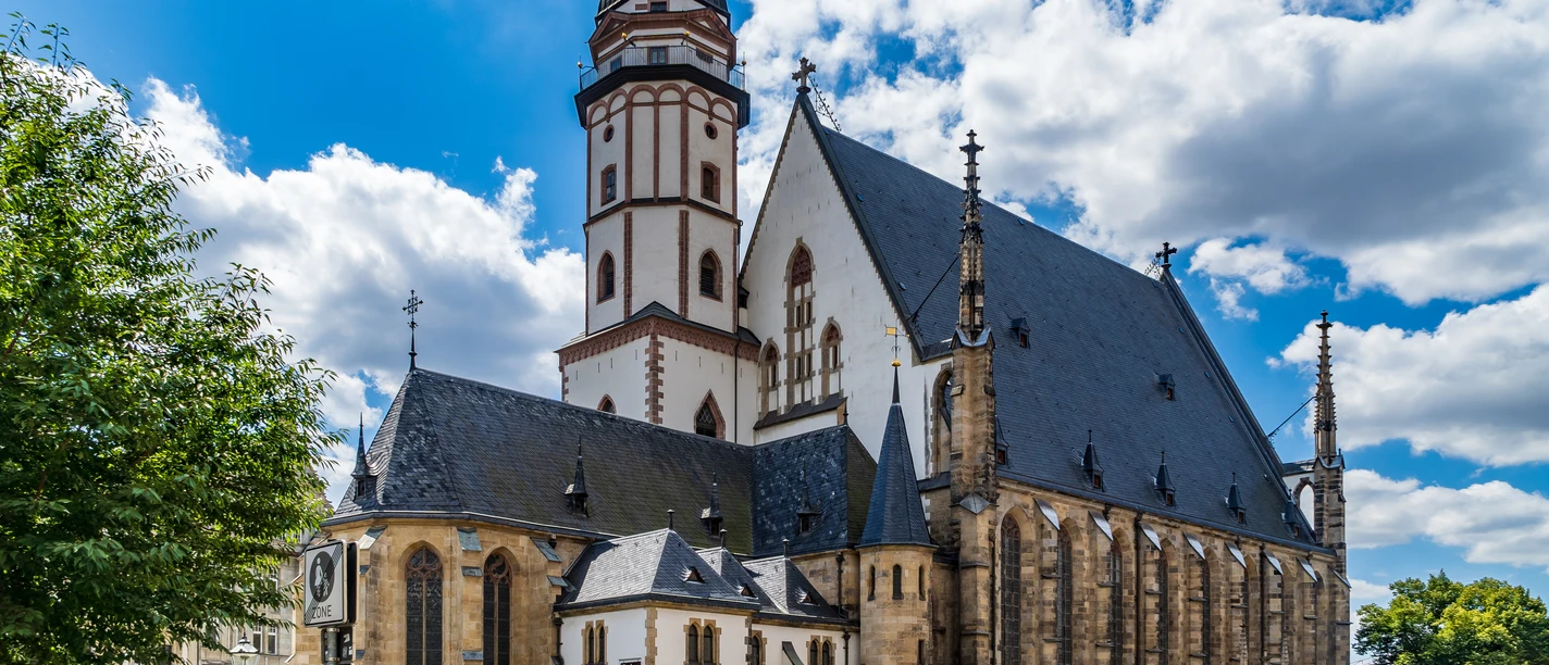 Thomaskirche in Leipzig St. Thomas Church Leipzig.jpg Die Thomaskirche in Leipzig mit gotischer Architektur unter blauem Himmel und vorbeifahrenden Autos.
