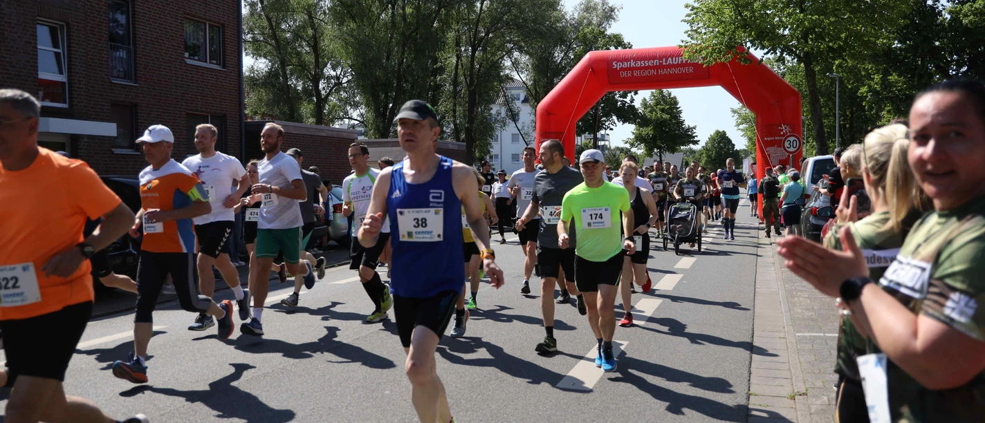 Stadtlauf Neustadt TSV Menschen unterschiedlichen Alters laufen konzentriert auf einer Straße unter einem roten Startbogen.