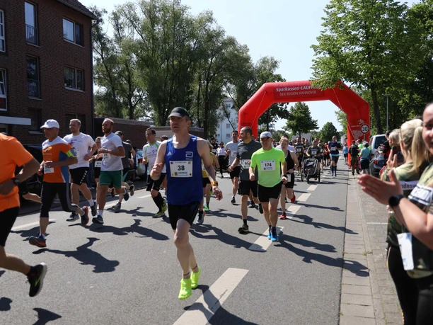 Menschen unterschiedlichen Alters laufen konzentriert auf einer Straße unter einem roten Startbogen.
