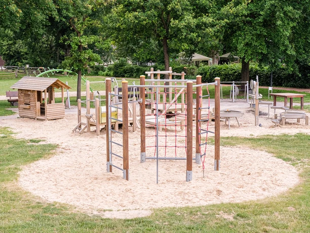 Spielplatz Museumshof Ein Spielplatz mit Holzhaus, Rutschbahn und Klettergerüst auf hellem Sandboden.
