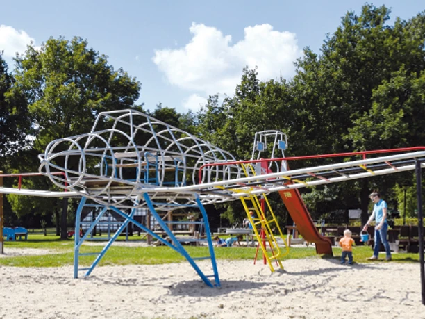 Spielplatz Museumshof Der Spielplatz zeigt eine große Kletteranlage in Form eines Flugzeugs auf hellem Sand.