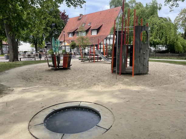 Spielplatz Alter Markt Ein Spielplatz mit Sandboden, Trampolin, Klettergerüst und Rutsche. Im Hintergrund Fachwerkhaus.
