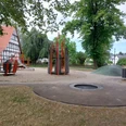 Spielplatz Alter Markt Ein moderner Spielplatz im Grünen mit Klettergerüst, Rutsche und Karussell. Ein Fachwerkhaus im Hintergrund.