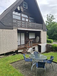 Balkon FeWo 1 u. 2 Rückansicht eines zweistöckigen Hauses mit Balkon, Terrasse, Hecke und runder Sitzgruppe im Garten.