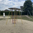 Metall-Klettergerüst mit Rutsche und Schaukel in einem Sandkasten auf einem Spielplatz.