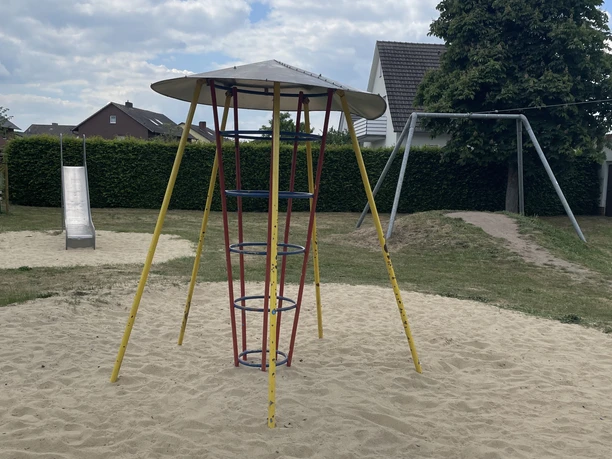 Metall-Klettergerüst mit Rutsche und Schaukel in einem Sandkasten auf einem Spielplatz.