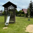 Auf dem Bild ist ein Spielplatz mit einer Rutsche zu sehen, umgeben von Rasen und einigen Bäumen.