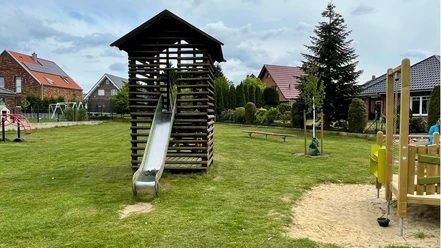 Specker Straße Auf dem Bild ist ein Spielplatz mit einer Rutsche zu sehen, umgeben von Rasen und einigen Bäumen.