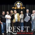 Ensemble Espelkamp, Neues Theater Auf dem Bild ist eine Gruppe von sieben Menschen auf einer Bühne zu sehen. Einige von ihnen lächeln in die Kamera. Im Hintergrund steht der Schriftzug "RESET - Alles auf Anfang!" prominent im Vordergrund.