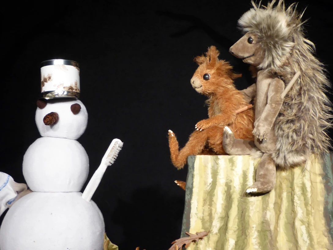 Herr Eichhorn und der erste Schnee Zwei Plüschfiguren, ein Eichhörnchen und ein Igel, betrachten einen Schneemann mit Zahnbürste im Arm.