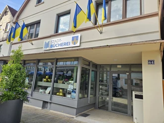 Bad Driburg_Stadtbücherei Stadtbücherei Bad Driburg mit gelb-blauen Fahnen, moderner Eingang und klaren Fensterfronten.