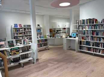 Innenaufnahme einer modernen Stadtbücherei mit hellen Regalen voller Bücher und einem Empfangstresen.