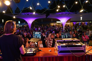 Silent Party 2025.jpg DJ legt bei bunter Silent Party auf, tanzende Gäste mit leuchtenden Kopfhörern unter Lichterketten