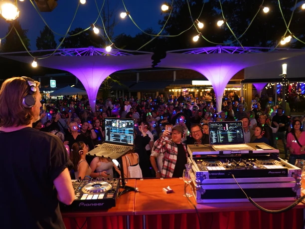 Silent Party 2025.jpg DJ legt bei bunter Silent Party auf, tanzende Gäste mit leuchtenden Kopfhörern unter Lichterketten