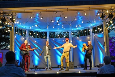 Comedy2025.jpg Vier Comedians stehen bei Dämmerung auf beleuchteter Bühne