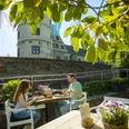 Paderborner-Land_Radfahren_Wewelsburg_Gastronomie_002 ©Kreis Paderborn, Sabrinity.jpg Zwei Menschen genießen eine Mahlzeit im Freien vor der historischen Wewelsburg bei Sonnenschein.
