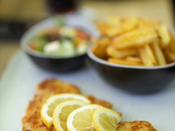 Panierter Schnitzel mit Zitronenscheiben, begleitet von Pommes frites und einem Schälchen Salat.