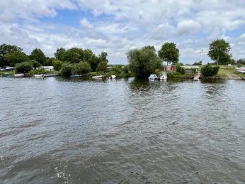 Weser-Camping Bollen Auf einem Flussabschnitt mit kleinen Booten und üppigem Grün bietet ein Ufer einen friedlichen Ausblick.