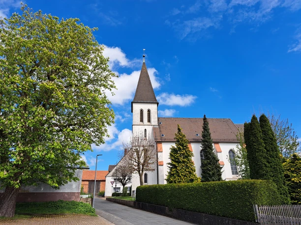 Katholische Kirche St. Bartholomäus zu Haarbrück Die katholische Kirche St. Bartholomäus in Haarbrück mit Spitzdach, umgeben von Bäumen, vor blauem Himmel.