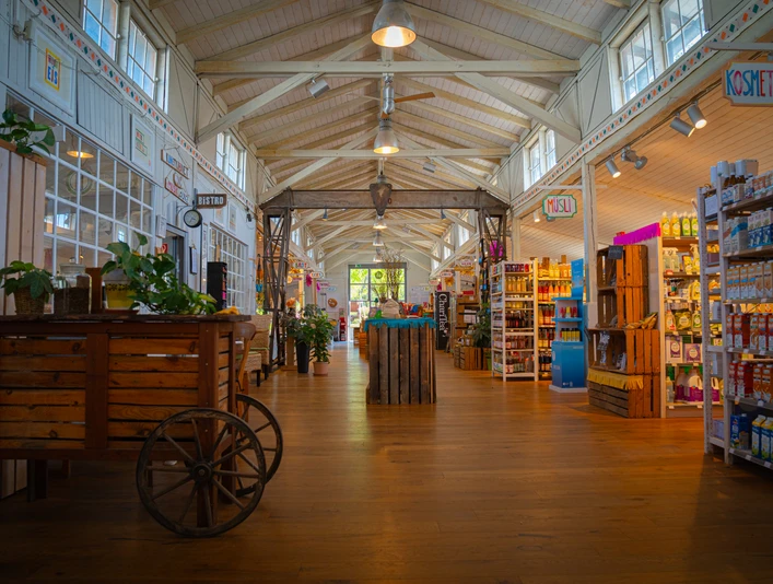 Bioladen Moorrübe Markthalle des Bioladen mit Lebensmittelregalen auf der rechten Seite und einem Holzkarren mit Pflanzen auf der Linken Seite.