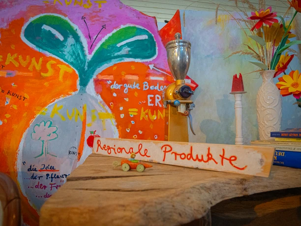 Regionale Produkte im Bioladen Moorrübe Holzplatte mit einem Schild, wo regionale Produkte steht. Die Wand dahinter ist künstlerisch gestaltet.