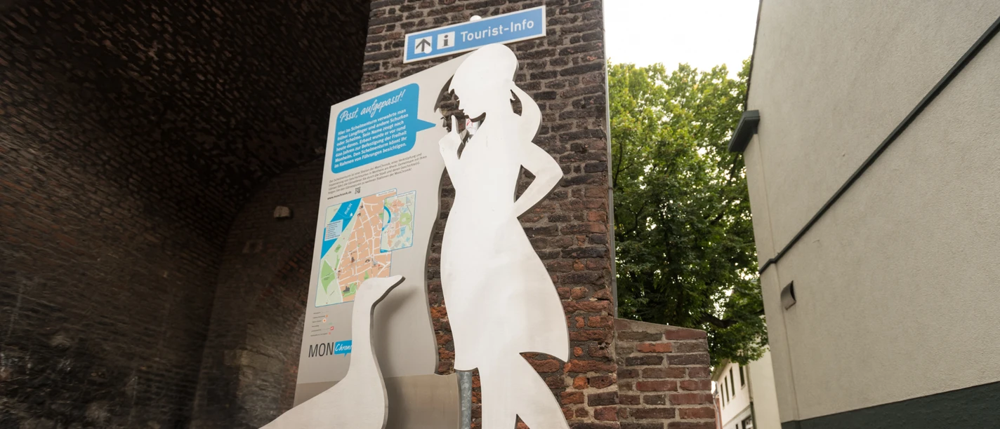 Säule der MonChronik vor dem Schelmenturm in Monheim am Rhein Silhouette einer Frau mit Gans in Metall vor dem historischen Schelmenturm in Monheim am Rhein.