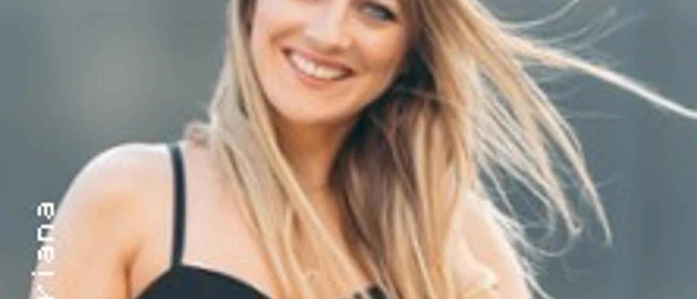 Eine Frau mit langen blonden Haaren lächelt in die Kamera. Sie trägt ein schwarzes Top.