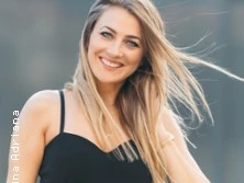 Eine Frau mit langen blonden Haaren lächelt in die Kamera. Sie trägt ein schwarzes Top.