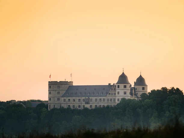 Wewelsburg im Sonnenuntergang Wewelsburg erhebt sich vor einem orangeroten Himmel, umgeben von üppigem Grün zum Sonnenuntergang.