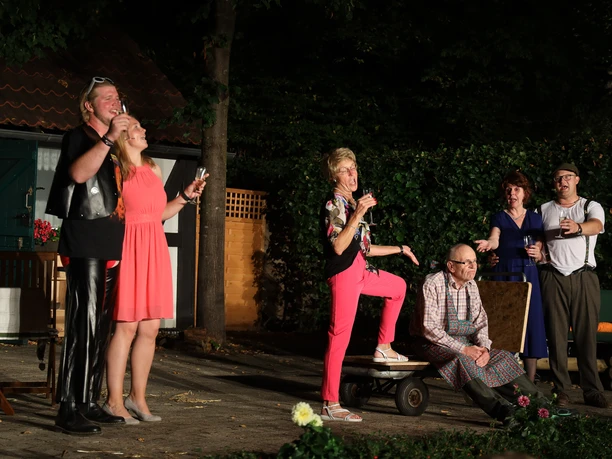 IMG_6966_E658D59C.JPG Eine Gruppe von sechs Personen in sommerlicher Kleidung genießt freudig eine Freilichttheateraufführung.