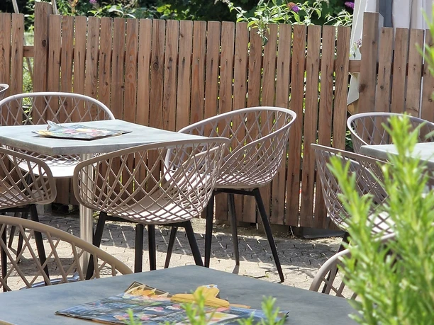 20250719_133132.jpg Gemütlicher Terrassenbereich mit modernen Metallstühlen und Holztischen, umgeben von grünen Pflanzen.