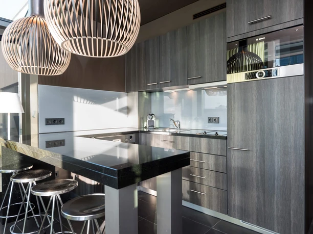 Hotelsuite mit angeschlossender Dachterasse im Adina Apartment Hotel Frankfurt Neue Oper Moderne Küche im Penthouse mit dunklen Holzmöbeln und Barbereich