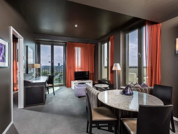 Hotel suite with adjoining roof terrace at the Adina Apartment Hotel Frankfurt Neue Oper Bright living area with dining table, desk and city view