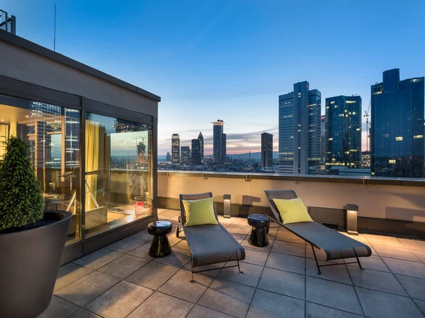 Hotelsuite mit angeschlossender Dachterasse im Adina Apartment Hotel Frankfurt Neue Oper Dachterrasse mit Liegen und Skylineblick bei Sonnenuntergang