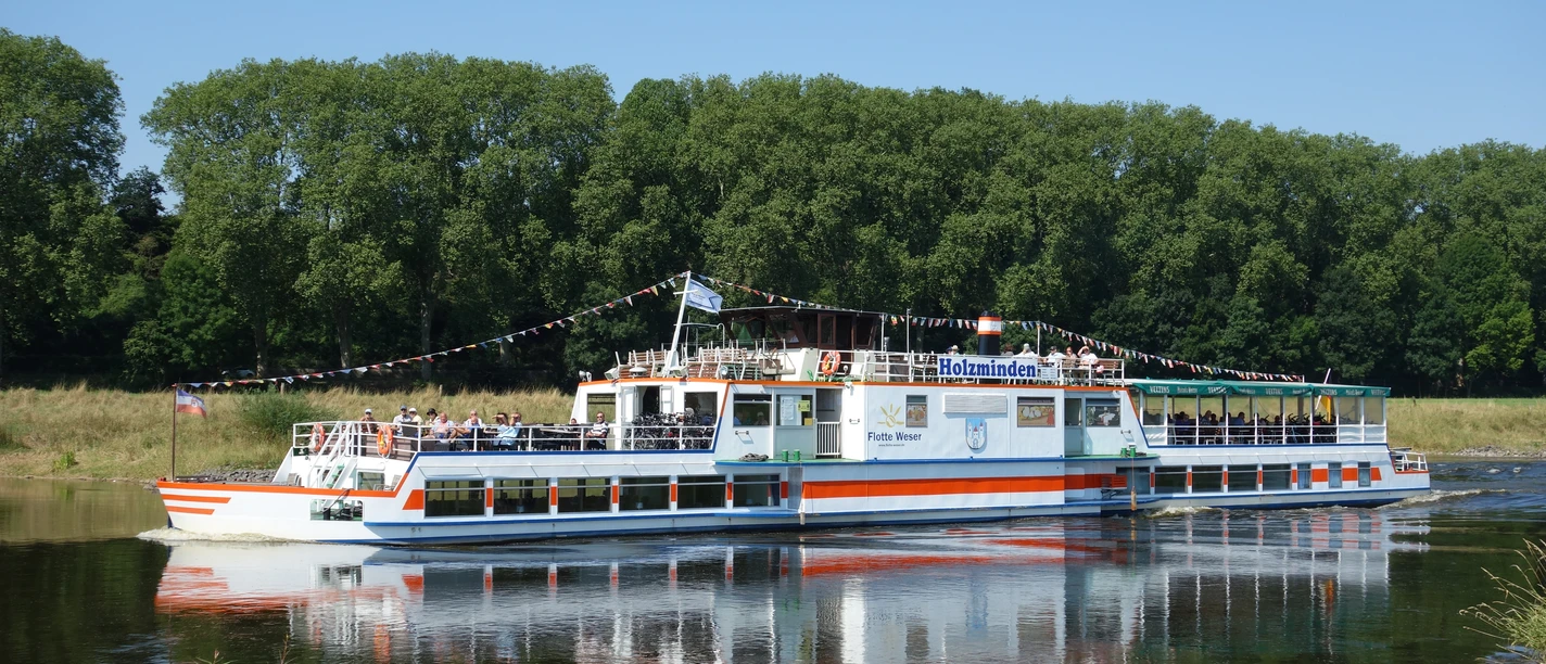 Flotte Weser The excursion boat Flotte Weser sails along a river lined with green trees.